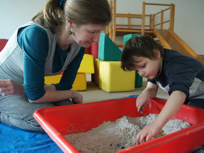 Pädagogin spielt mit Kind in der Sandwanne